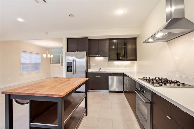 kitchen with dark brown cabinetry, wooden counters, decorative light fixtures, wall chimney exhaust hood, and appliances with stainless steel finishes