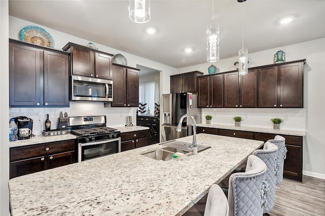 kitchen featuring hanging light fixtures, sink, appliances with stainless steel finishes, a breakfast bar, and light wood-type flooring