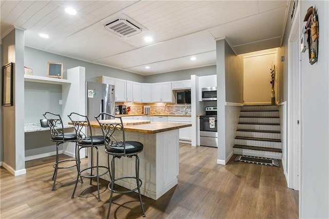 kitchen featuring visible vents, a breakfast bar, appliances with stainless steel finishes, wood finished floors, and wood counters