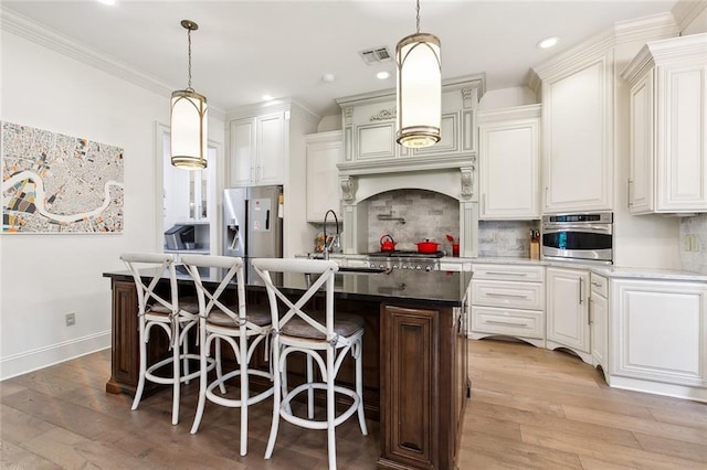 kitchen with sink, decorative backsplash, an island with sink, appliances with stainless steel finishes, and white cabinetry