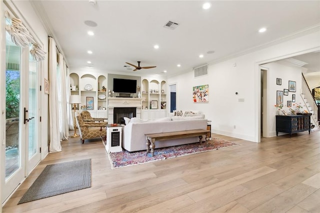 living room featuring french doors, crown molding, light hardwood / wood-style flooring, ceiling fan, and built in features