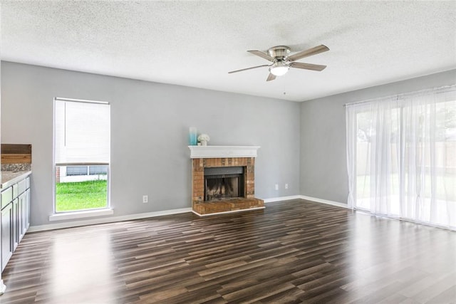 unfurnished living room with a brick fireplace, ceiling fan, dark wood-type flooring, and a textured ceiling