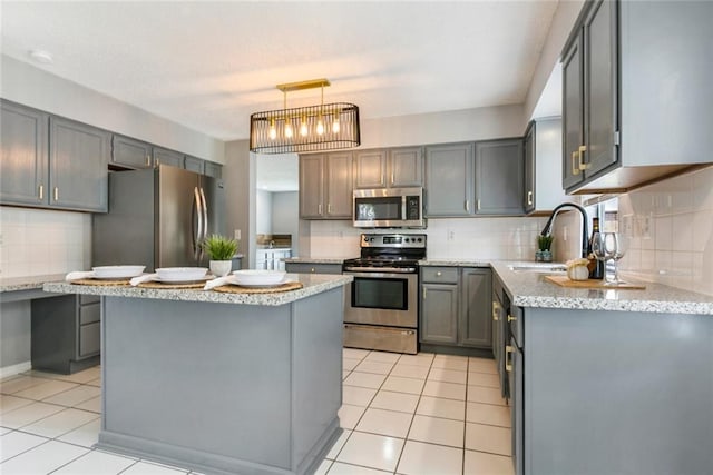 kitchen with appliances with stainless steel finishes, hanging light fixtures, gray cabinetry, a center island, and sink