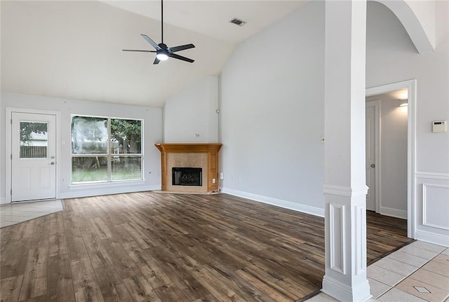 unfurnished living room with high vaulted ceiling, a fireplace, light hardwood / wood-style flooring, ceiling fan, and decorative columns