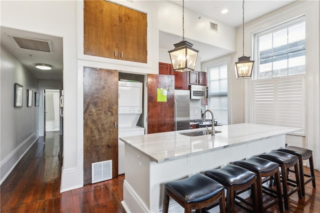 kitchen with appliances with stainless steel finishes, hanging light fixtures, a breakfast bar area, dark hardwood / wood-style flooring, and stacked washer / drying machine