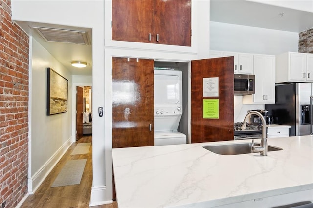 kitchen with light hardwood / wood-style floors, light stone countertops, stainless steel appliances, stacked washer and dryer, and sink