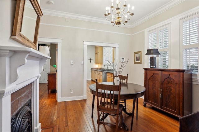 dining room featuring sink, a chandelier, dark wood-type flooring, a fireplace, and crown molding