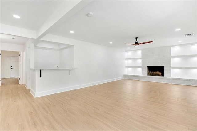 unfurnished living room featuring light hardwood / wood-style floors, beam ceiling, a fireplace, ceiling fan, and built in features