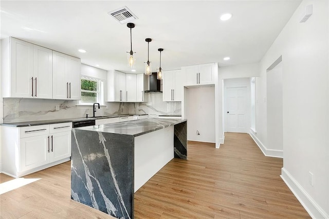 kitchen featuring white cabinets, light hardwood / wood-style flooring, decorative light fixtures, wall chimney range hood, and a center island