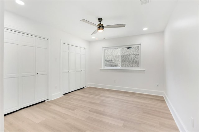 unfurnished bedroom featuring ceiling fan, multiple closets, and light wood-type flooring