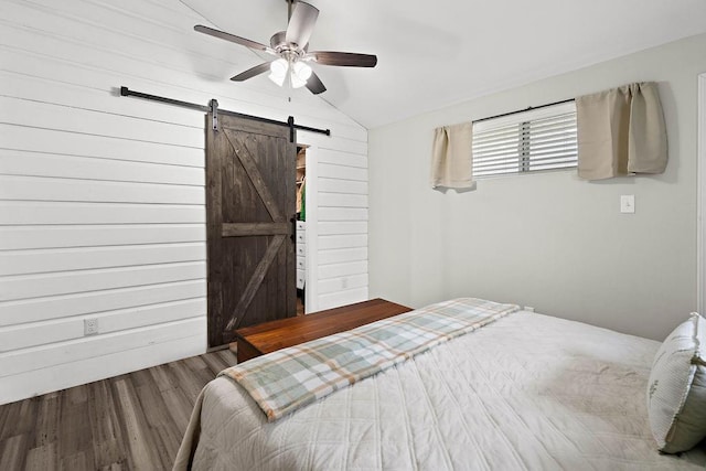 bedroom featuring ceiling fan, wood walls, wood-type flooring, a barn door, and vaulted ceiling