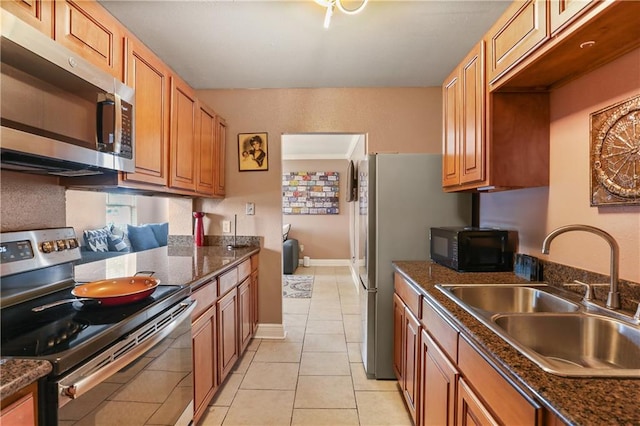 kitchen with light tile patterned flooring, appliances with stainless steel finishes, sink, and dark stone counters