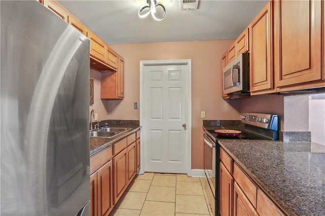 kitchen with sink, stainless steel appliances, light tile patterned floors, and dark stone counters