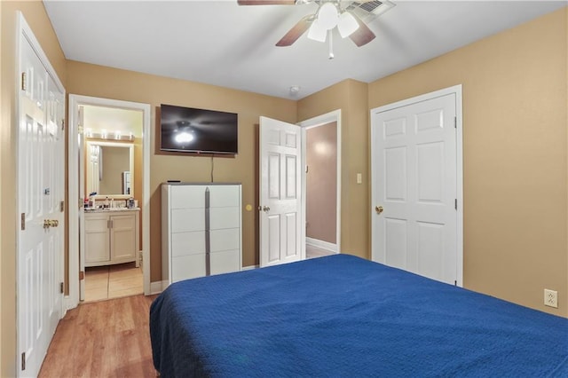 bedroom with light wood-type flooring, ceiling fan, ensuite bathroom, and sink