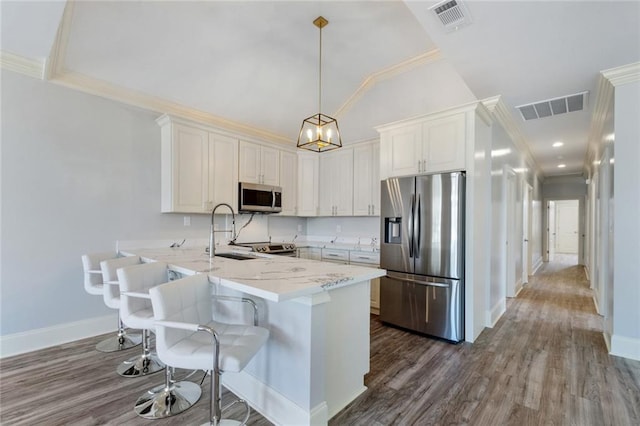 kitchen featuring appliances with stainless steel finishes, hanging light fixtures, white cabinetry, kitchen peninsula, and hardwood / wood-style floors