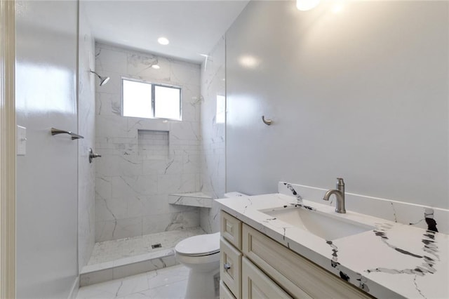 bathroom with tiled shower, vanity, and toilet