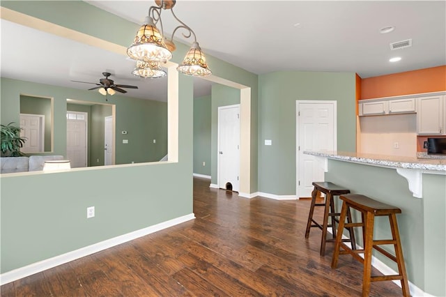 kitchen with pendant lighting, white cabinetry, ceiling fan with notable chandelier, a kitchen bar, and dark hardwood / wood-style flooring