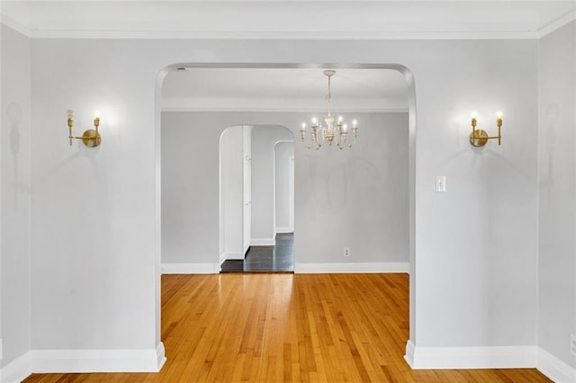 empty room with ornamental molding, a chandelier, and hardwood / wood-style flooring