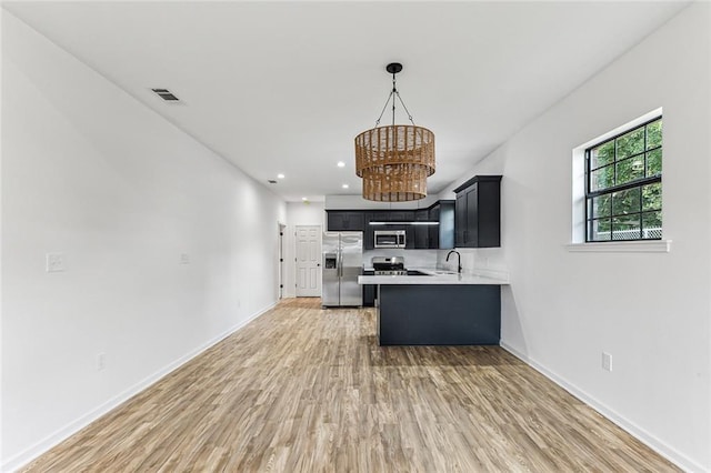 kitchen with wood-type flooring, kitchen peninsula, appliances with stainless steel finishes, and hanging light fixtures