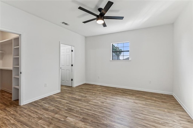 unfurnished bedroom featuring a spacious closet, ceiling fan, and hardwood / wood-style flooring