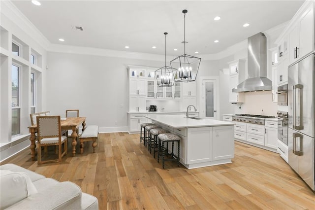 kitchen with light hardwood / wood-style floors, a kitchen island with sink, wall chimney range hood, and white cabinets