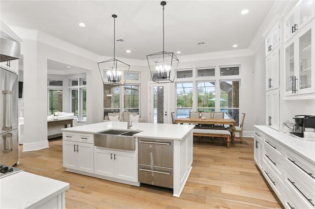 kitchen with pendant lighting, light hardwood / wood-style floors, sink, an island with sink, and white cabinetry