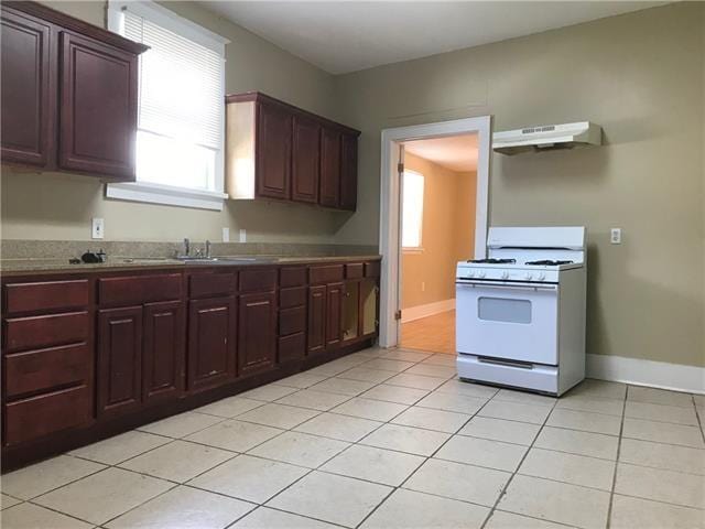 kitchen with ventilation hood, white gas range, sink, and light tile patterned floors