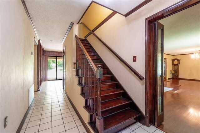 stairs featuring a textured ceiling, ornamental molding, an inviting chandelier, and hardwood / wood-style flooring