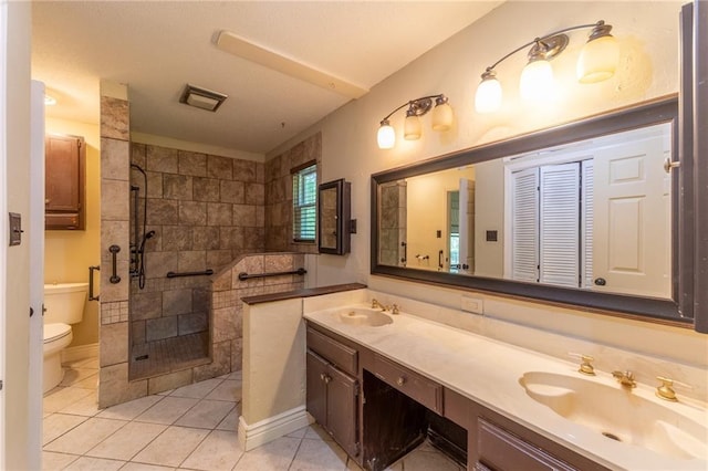 bathroom featuring tile patterned flooring, tiled shower, vanity, and toilet