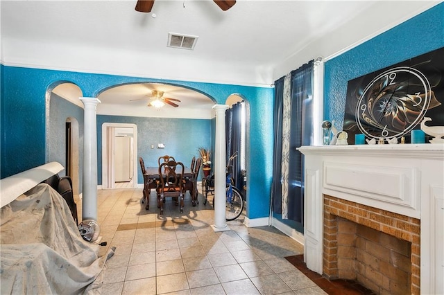 tiled foyer entrance with a brick fireplace, ceiling fan, and ornate columns