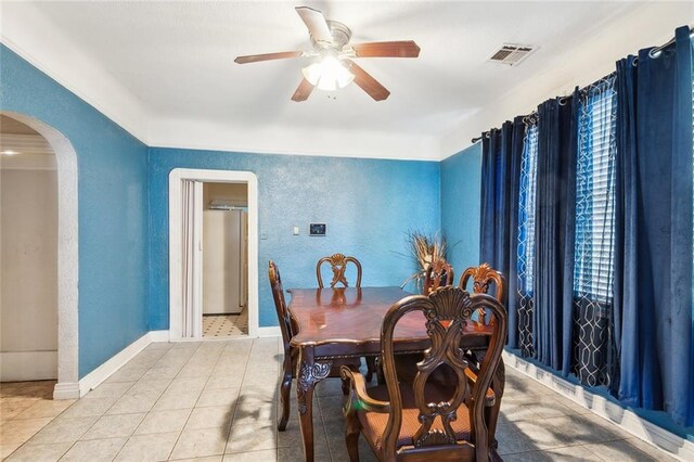 tiled dining area with visible vents, baseboards, ceiling fan, arched walkways, and a textured wall