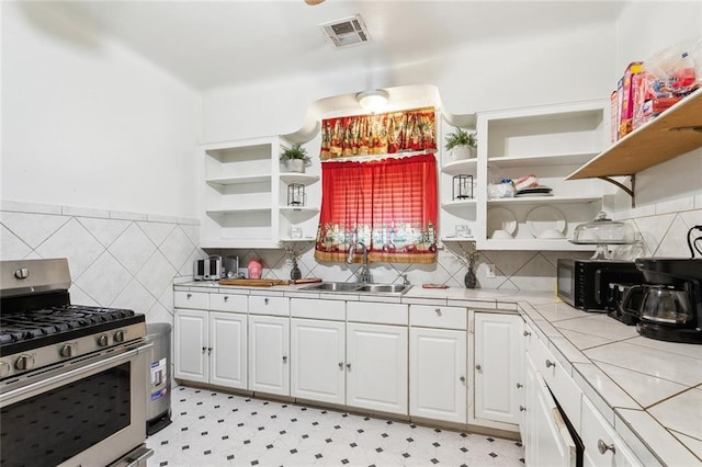 kitchen with stainless steel gas range oven, tile counters, open shelves, a sink, and visible vents