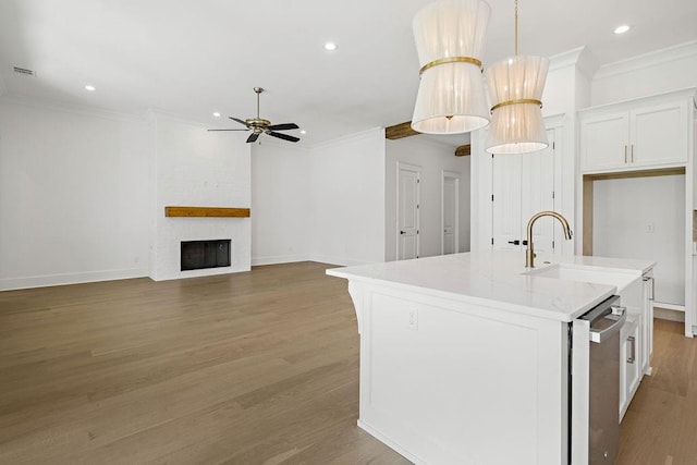 kitchen featuring hardwood / wood-style flooring, sink, an island with sink, white cabinets, and a fireplace