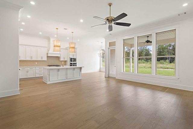 unfurnished living room with ceiling fan, sink, crown molding, and light hardwood / wood-style floors