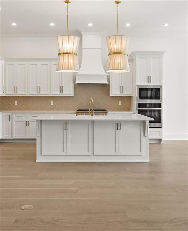 kitchen with white cabinets, stainless steel appliances, hanging light fixtures, and custom range hood