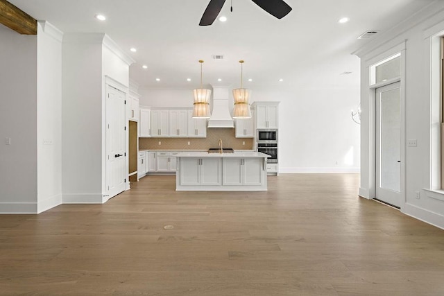 kitchen with decorative backsplash, white cabinetry, stainless steel appliances, light hardwood / wood-style flooring, and a center island with sink