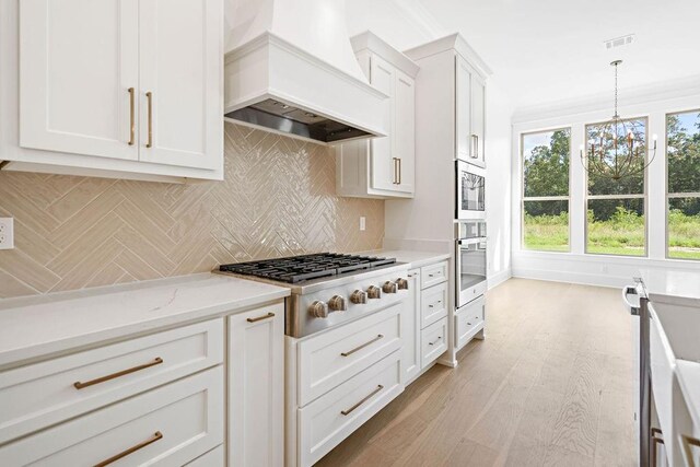 kitchen featuring white cabinets, pendant lighting, light hardwood / wood-style flooring, stainless steel gas stovetop, and premium range hood