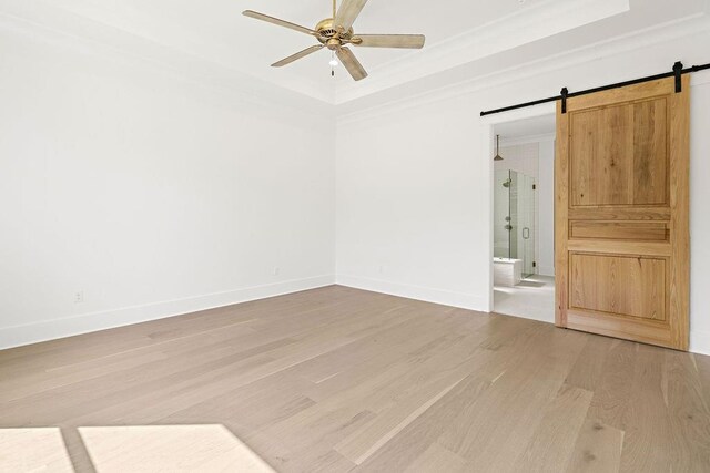 empty room with ceiling fan, a raised ceiling, ornamental molding, hardwood / wood-style flooring, and a barn door