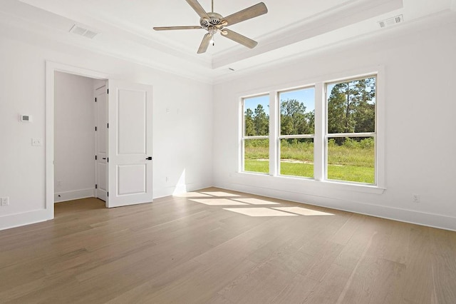 empty room featuring wood-type flooring, ceiling fan, a raised ceiling, and crown molding