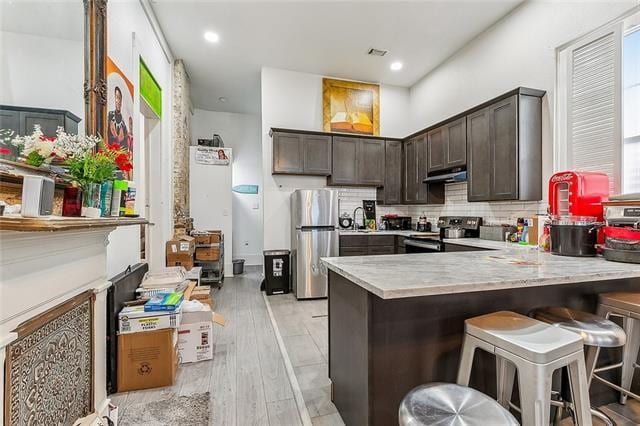 kitchen featuring dark brown cabinets, a breakfast bar area, kitchen peninsula, light hardwood / wood-style flooring, and stainless steel appliances