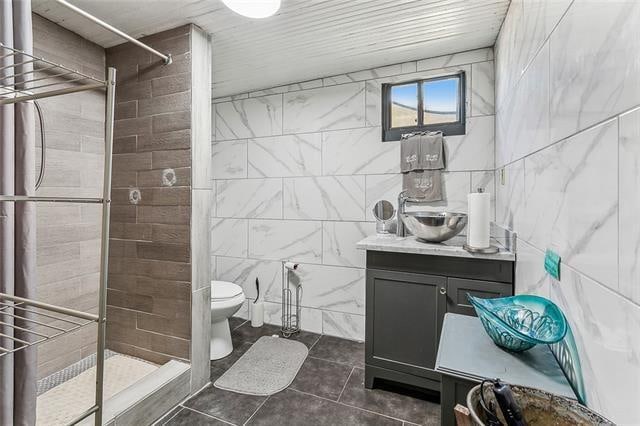 bathroom with tile walls, walk in shower, vanity, and toilet