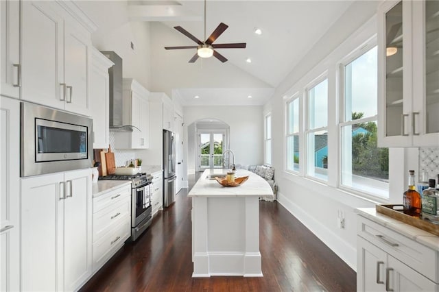 kitchen with ceiling fan, white cabinets, sink, wall chimney range hood, and appliances with stainless steel finishes