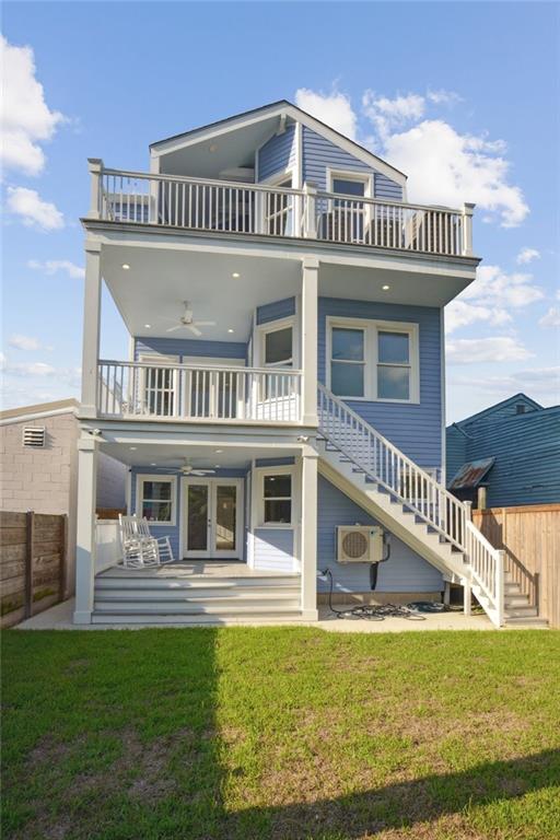 rear view of property with a balcony, ceiling fan, and a yard