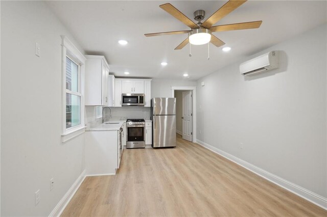 kitchen with appliances with stainless steel finishes, white cabinets, an AC wall unit, light hardwood / wood-style flooring, and sink