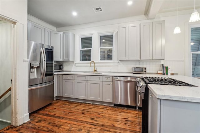 kitchen with hanging light fixtures, dark wood-type flooring, light stone counters, stainless steel appliances, and sink