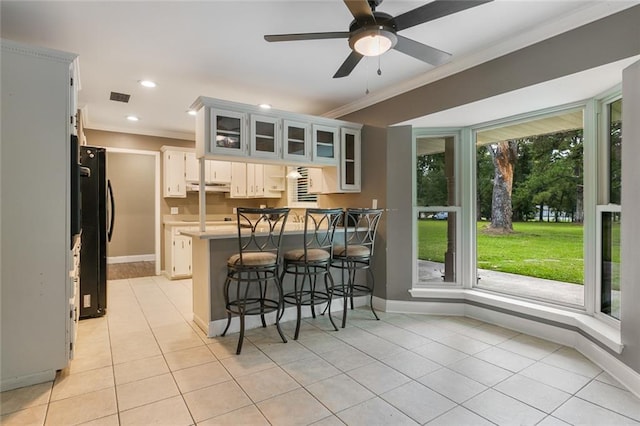 kitchen with white cabinets, kitchen peninsula, a kitchen bar, ceiling fan, and refrigerator