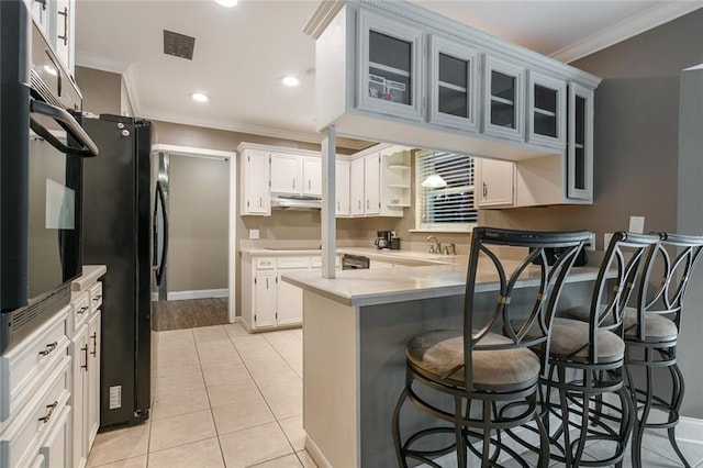 kitchen featuring black fridge, a breakfast bar area, white cabinets, light tile patterned floors, and crown molding