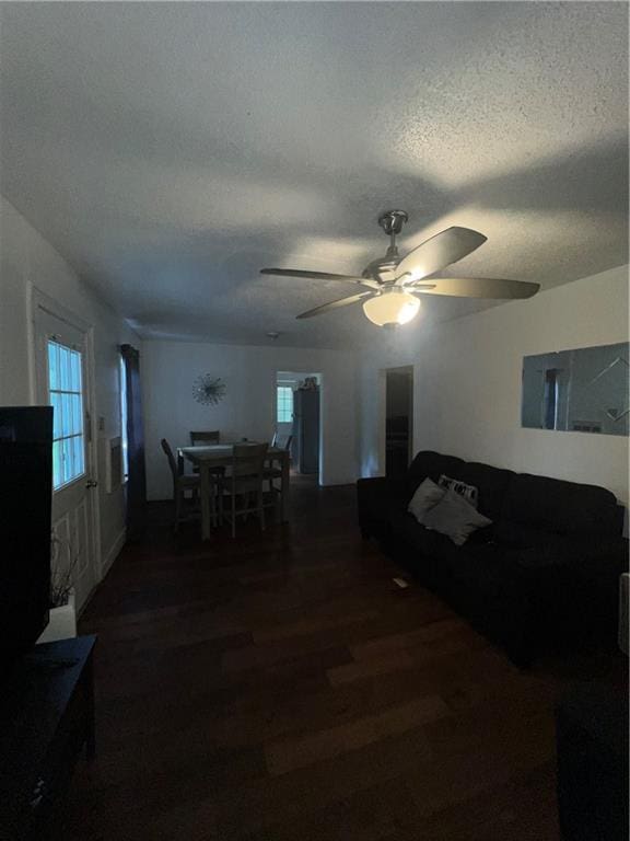 living room with a wealth of natural light, ceiling fan, dark hardwood / wood-style floors, and a textured ceiling