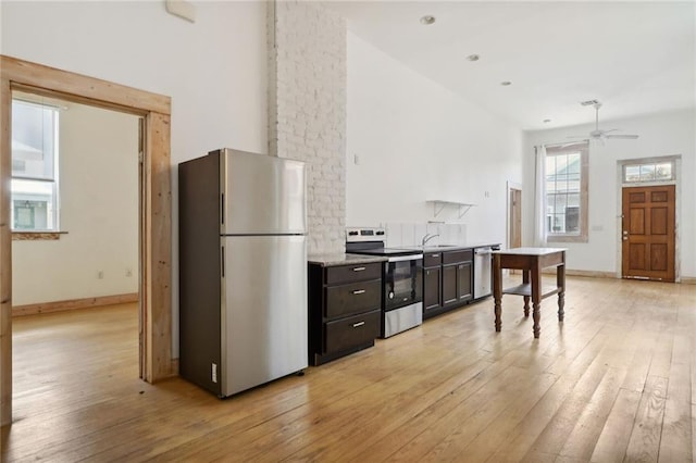 kitchen featuring appliances with stainless steel finishes, light hardwood / wood-style floors, ceiling fan, and a high ceiling