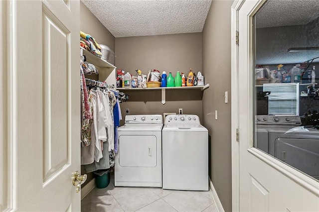 clothes washing area with washer and dryer, a textured ceiling, and light tile patterned floors